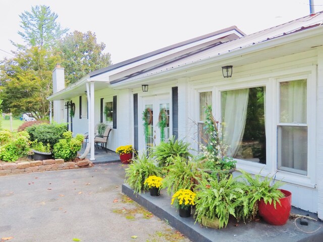 doorway to property with a porch, a chimney, and metal roof