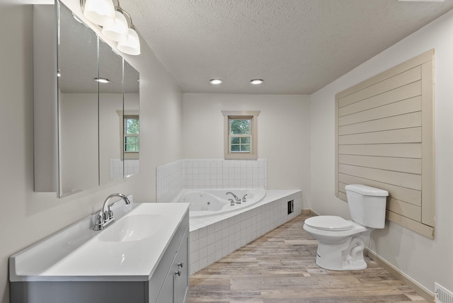 bathroom featuring a textured ceiling, vanity, tiled bath, toilet, and hardwood / wood-style flooring