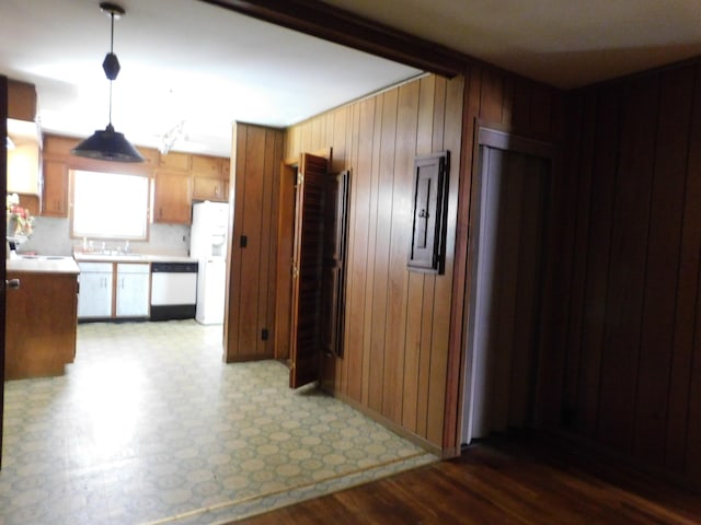 kitchen featuring wooden walls, electric panel, dishwashing machine, hanging light fixtures, and white refrigerator