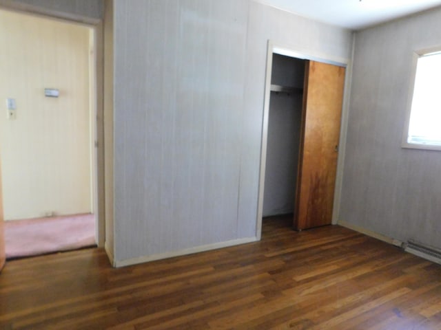 unfurnished bedroom featuring dark wood-type flooring, a closet, and a baseboard radiator