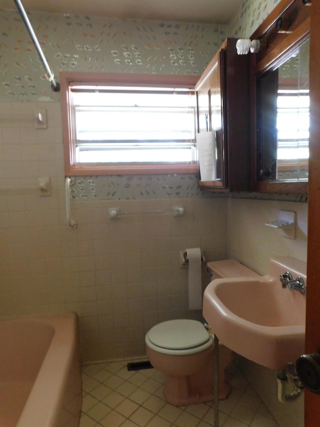 full bathroom with tile patterned floors, tile walls, toilet, and a healthy amount of sunlight