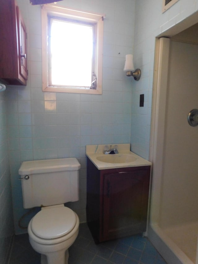 bathroom with vanity, tile patterned flooring, tile walls, toilet, and a shower