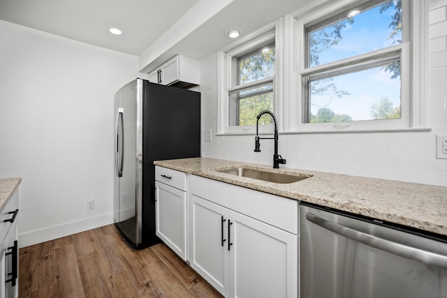 kitchen featuring white cabinets, light wood-type flooring, light stone countertops, stainless steel appliances, and sink