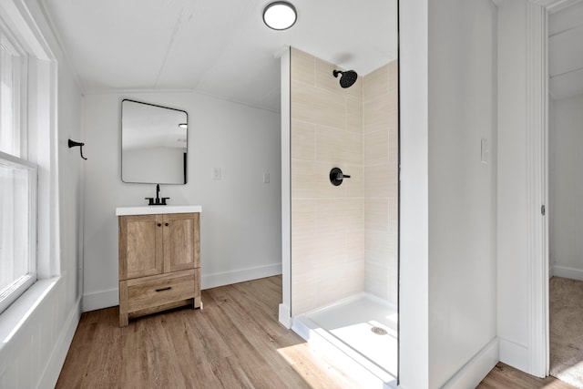 bathroom with lofted ceiling, hardwood / wood-style flooring, a tile shower, and vanity