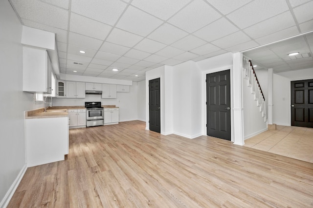 kitchen featuring a paneled ceiling, stainless steel range, light wood-type flooring, and white cabinets