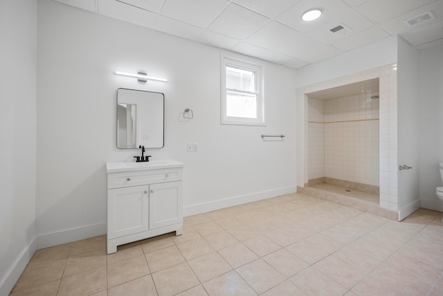 bathroom with toilet, tile patterned flooring, vanity, a tile shower, and a paneled ceiling