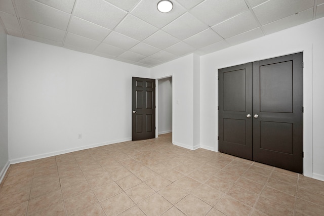 unfurnished bedroom with light tile patterned floors, a closet, and a drop ceiling