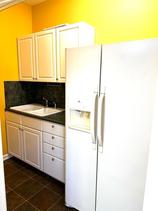 kitchen featuring sink, white cabinets, decorative backsplash, dark tile patterned floors, and white fridge with ice dispenser