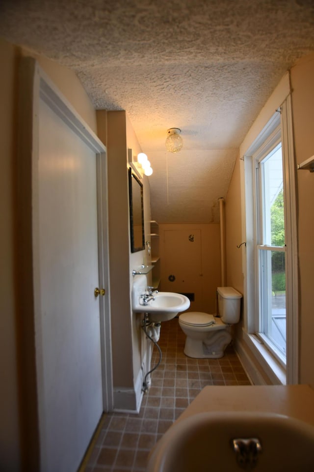 half bathroom featuring a textured ceiling, toilet, a sink, vaulted ceiling, and tile patterned flooring