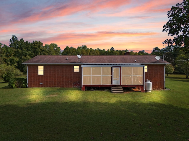 back house at dusk featuring a sunroom and a lawn