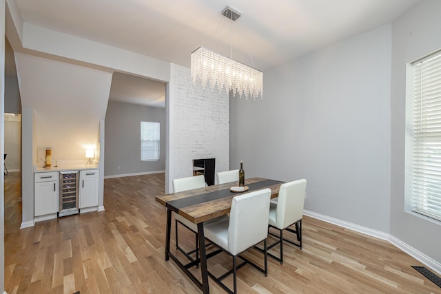 dining area featuring light wood finished floors, visible vents, baseboards, a chandelier, and beverage cooler