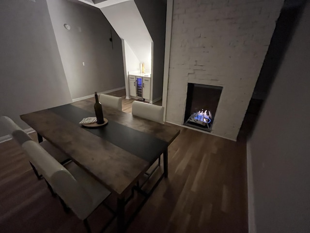 dining space featuring beverage cooler, a large fireplace, wood finished floors, and baseboards