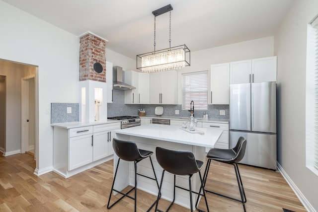 kitchen featuring a breakfast bar, wall chimney range hood, stainless steel appliances, light wood finished floors, and light countertops