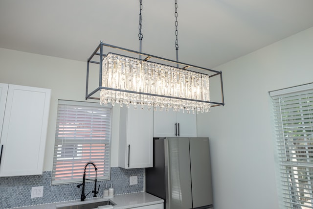 kitchen featuring a sink, backsplash, freestanding refrigerator, white cabinets, and light countertops