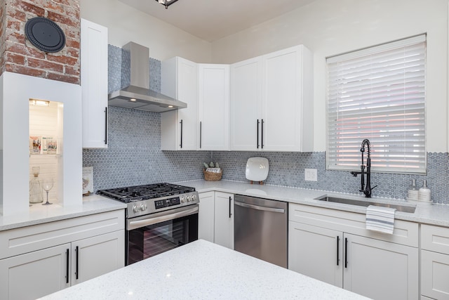 kitchen with decorative backsplash, stainless steel appliances, wall chimney range hood, white cabinetry, and a sink