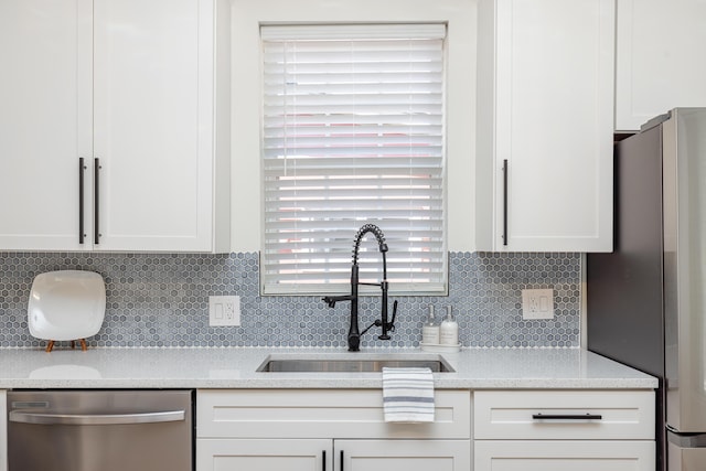 kitchen with stainless steel appliances, backsplash, white cabinetry, a sink, and light stone countertops