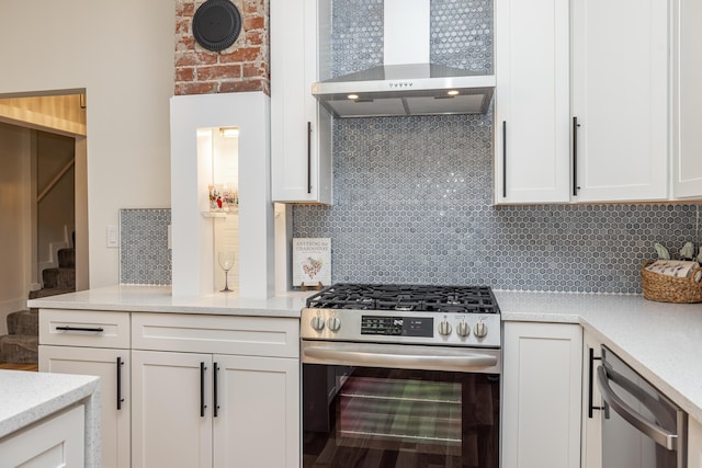 kitchen with decorative backsplash, wall chimney exhaust hood, appliances with stainless steel finishes, light stone countertops, and white cabinetry