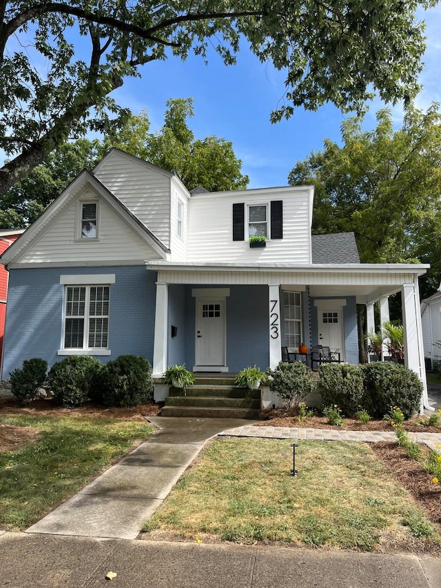 view of front facade featuring brick siding, covered porch, and a front yard