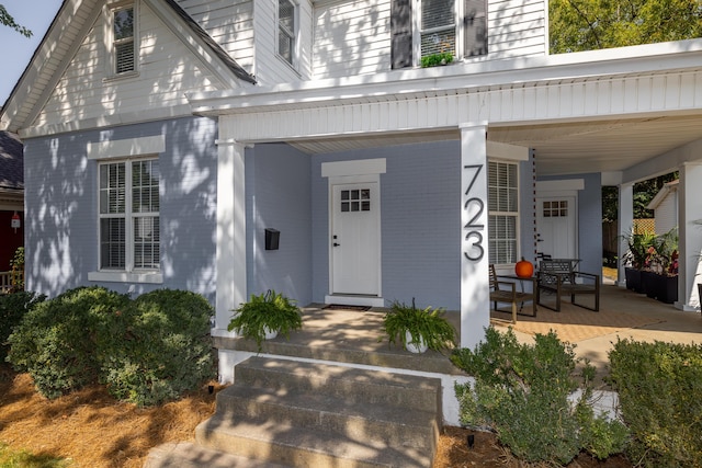 property entrance featuring a porch and brick siding