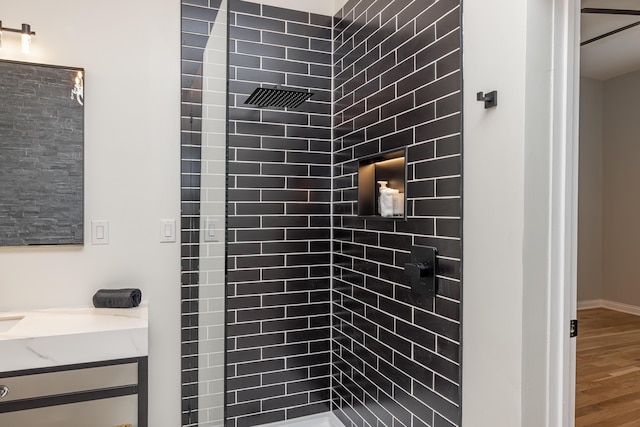 bathroom featuring a tile shower, wood finished floors, and vanity