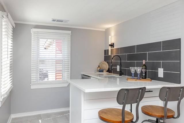 kitchen with visible vents, a sink, a kitchen breakfast bar, crown molding, and decorative backsplash