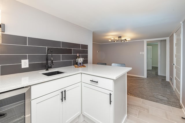 kitchen featuring tasteful backsplash, beverage cooler, a peninsula, white cabinetry, and a sink