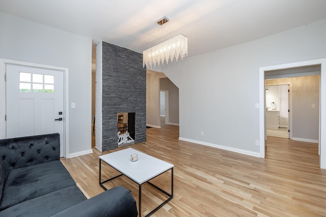 living room featuring a stone fireplace, light wood finished floors, an inviting chandelier, and baseboards