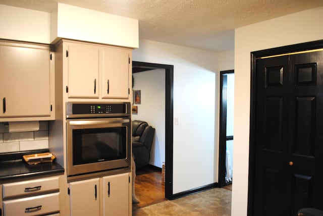 kitchen featuring tasteful backsplash, white cabinetry, stainless steel oven, and a textured ceiling