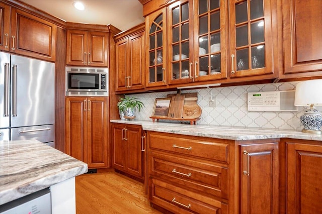 kitchen featuring appliances with stainless steel finishes, light wood-type flooring, and light stone countertops