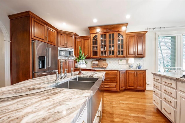 kitchen with light stone counters, sink, light hardwood / wood-style flooring, backsplash, and stainless steel appliances