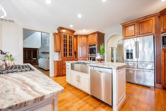 kitchen featuring light wood-type flooring, a center island with sink, built in appliances, and sink