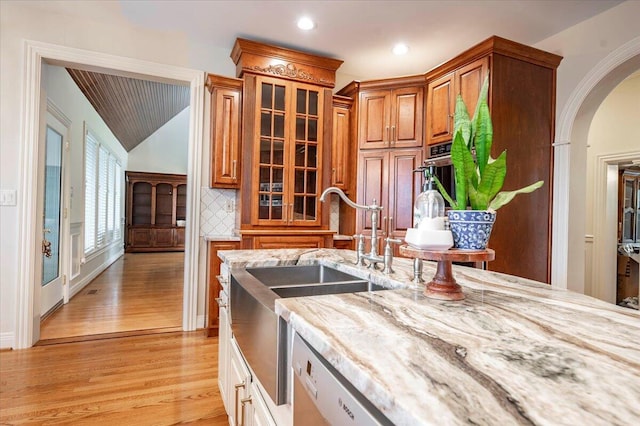 kitchen featuring vaulted ceiling, tasteful backsplash, light stone countertops, stainless steel appliances, and light wood-type flooring