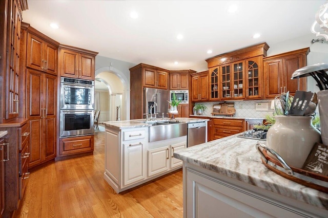 kitchen featuring decorative backsplash, light hardwood / wood-style floors, stainless steel appliances, a kitchen island with sink, and sink