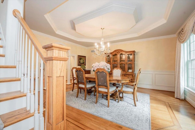 dining area featuring light wood-type flooring, crown molding, a tray ceiling, and a notable chandelier