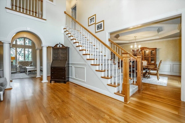 foyer featuring crown molding, a high ceiling, an inviting chandelier, hardwood / wood-style flooring, and decorative columns