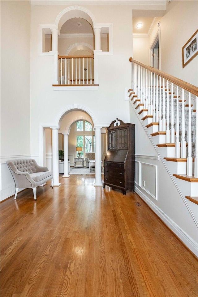 interior space featuring wood-type flooring, decorative columns, crown molding, and a towering ceiling