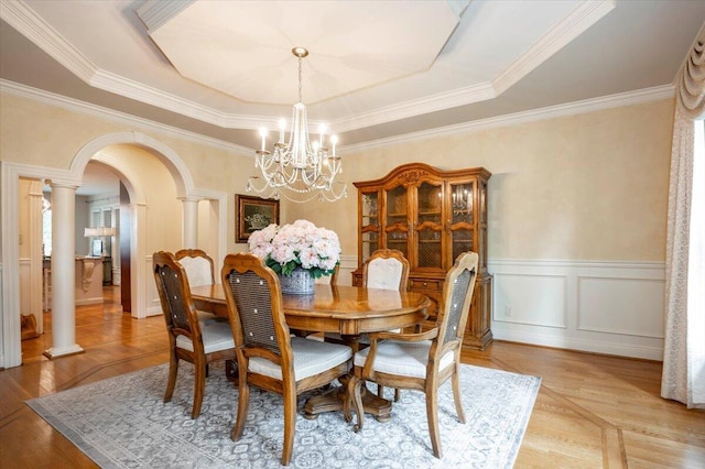 dining space with a notable chandelier, light hardwood / wood-style flooring, a raised ceiling, crown molding, and ornate columns