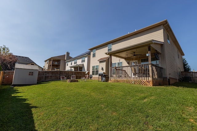 rear view of property featuring a yard, a deck, a storage unit, and ceiling fan