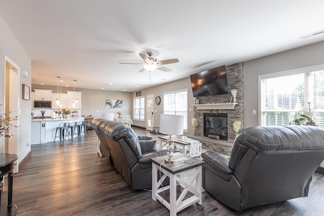 living room featuring dark wood-type flooring, ceiling fan, a fireplace, and a healthy amount of sunlight