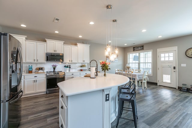 kitchen featuring white cabinets, decorative light fixtures, stainless steel appliances, and an island with sink