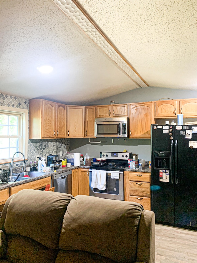 kitchen featuring light wood-type flooring, a textured ceiling, stainless steel appliances, sink, and vaulted ceiling