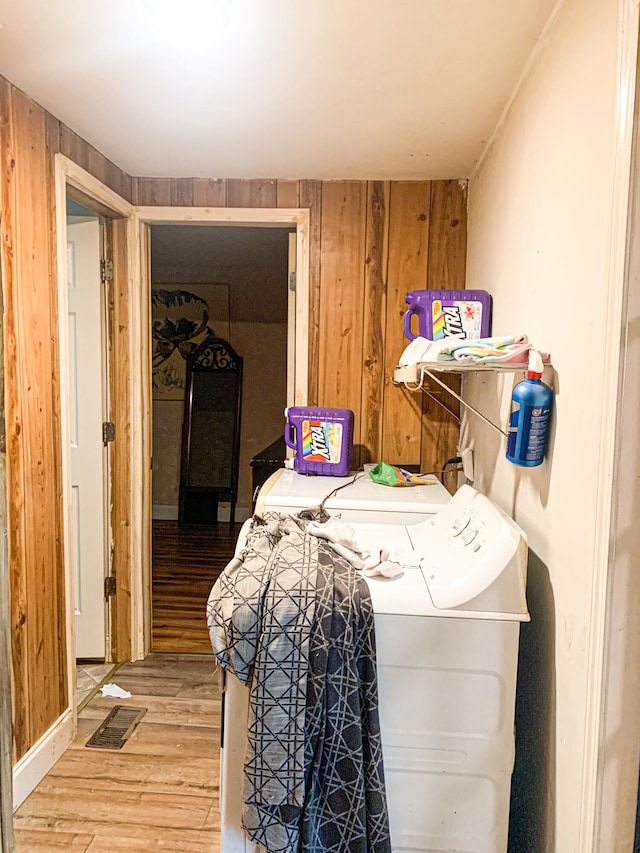 clothes washing area with wood-type flooring, washer and dryer, and wooden walls