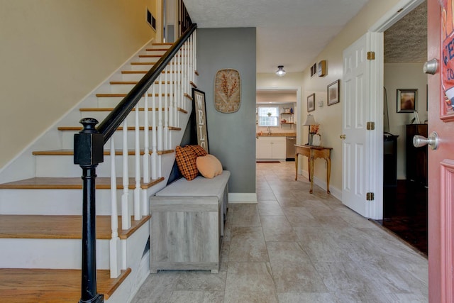 stairway with a textured ceiling, sink, and tile patterned flooring