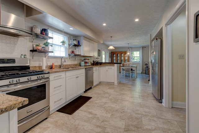 kitchen with decorative light fixtures, sink, wall chimney exhaust hood, appliances with stainless steel finishes, and white cabinets