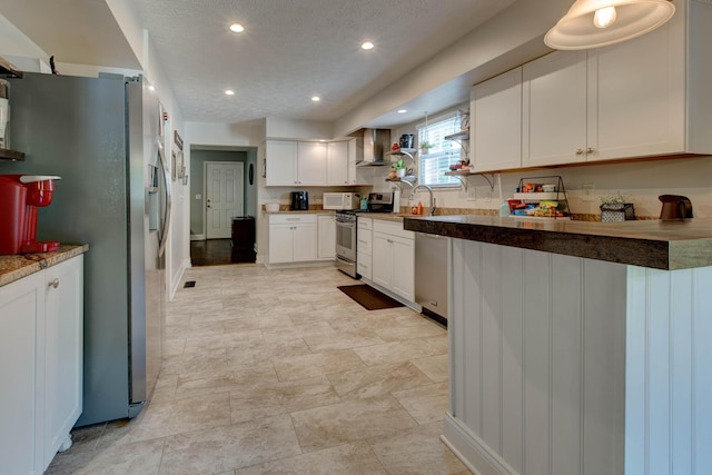 kitchen with appliances with stainless steel finishes, white cabinetry, sink, wall chimney range hood, and a textured ceiling