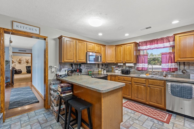 kitchen featuring a textured ceiling, sink, kitchen peninsula, a kitchen breakfast bar, and appliances with stainless steel finishes