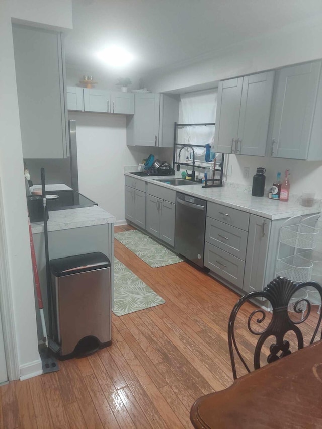 kitchen with light stone countertops, gray cabinetry, sink, light hardwood / wood-style flooring, and dishwasher