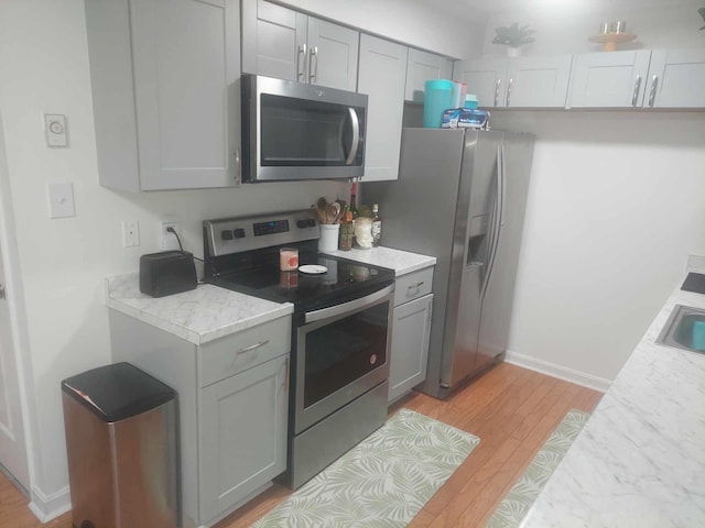 kitchen with appliances with stainless steel finishes, light wood-type flooring, and gray cabinetry