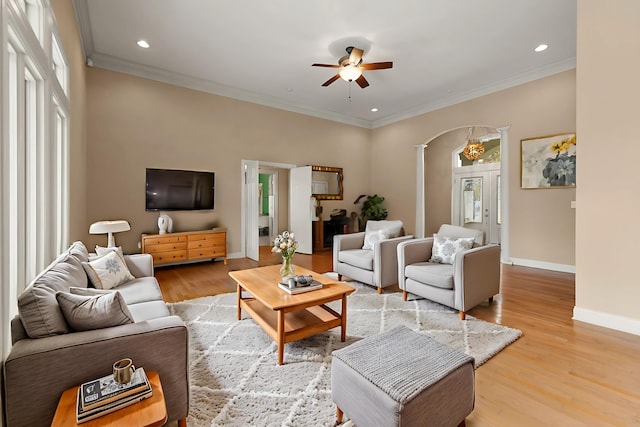 living room with light wood-type flooring, ornamental molding, ceiling fan, and ornate columns