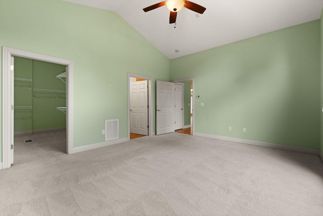 unfurnished bedroom featuring a walk in closet, high vaulted ceiling, light colored carpet, a closet, and ceiling fan